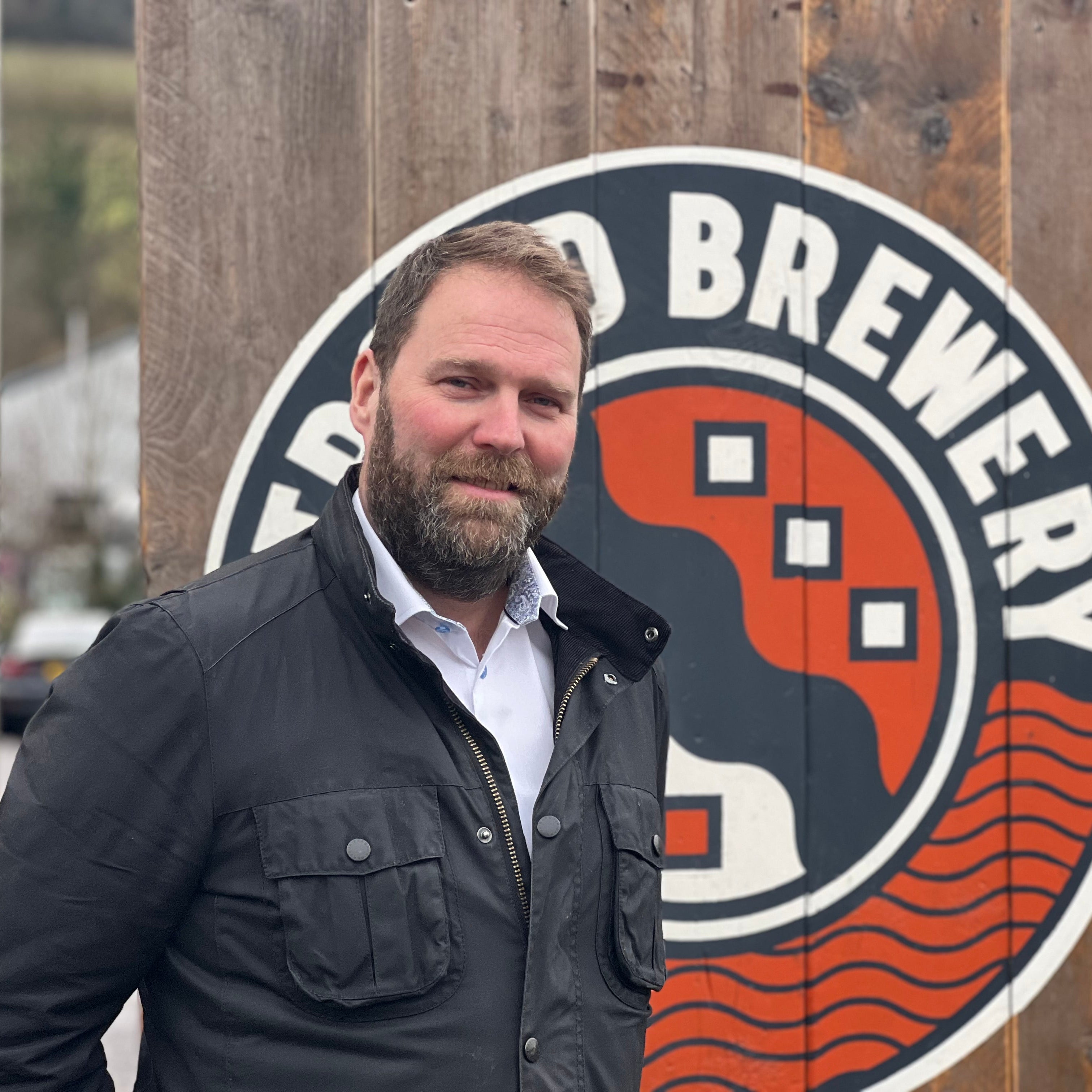 Daniel Morris standing in front of a brewery sign with a logo on a wooden background