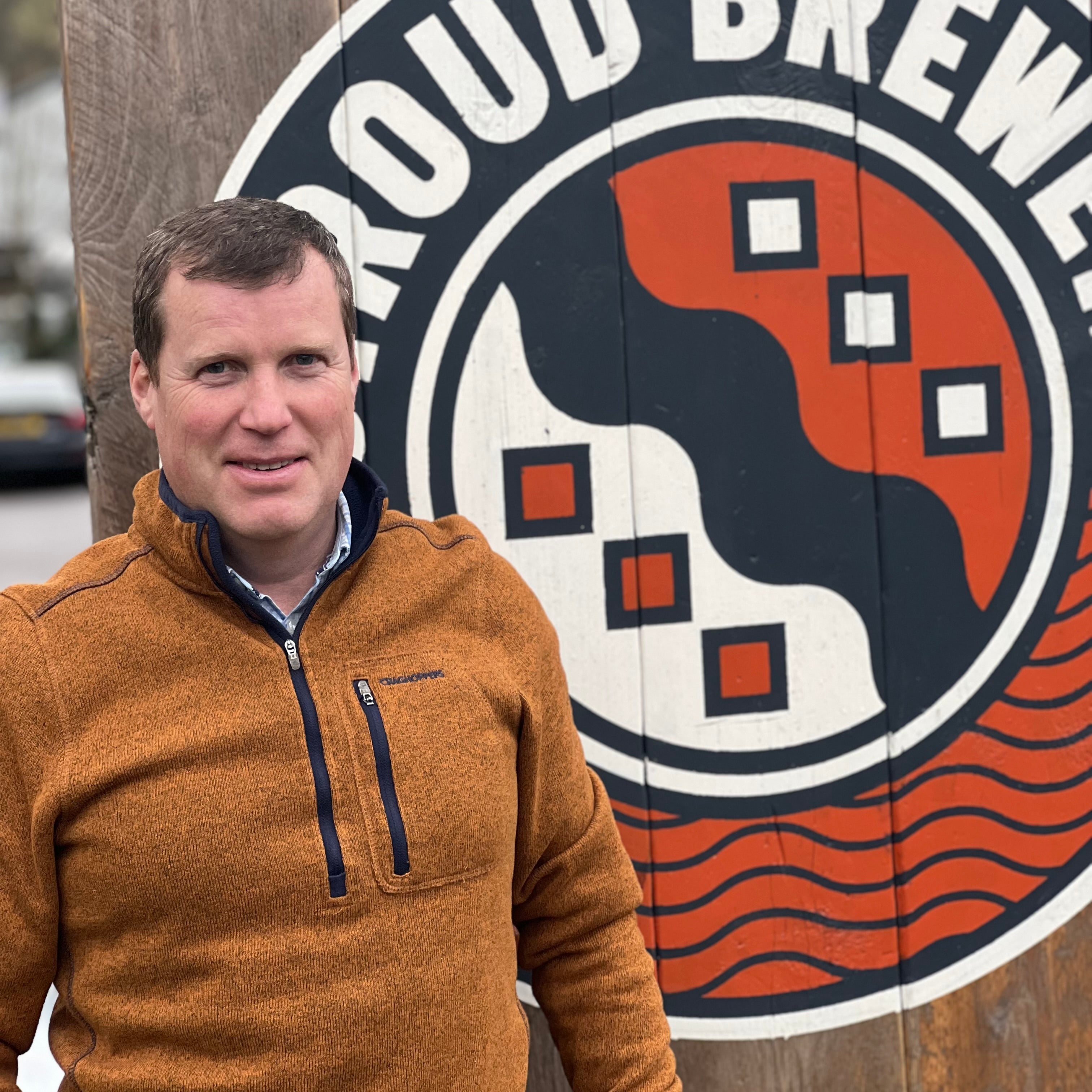 Benjamin Morris standing in front of a wooden sign with a logo